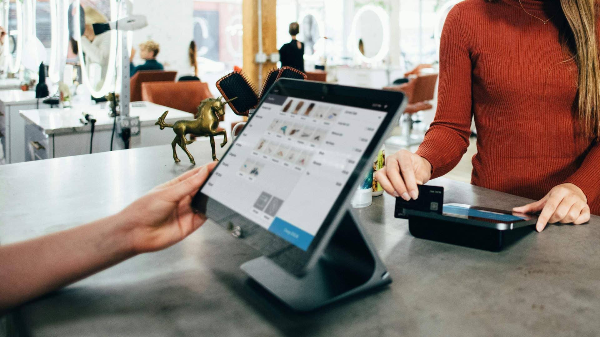 Small business owner processing a customer payment on a tablet POS system in a modern salon, highlighting technology in everyday business operations.