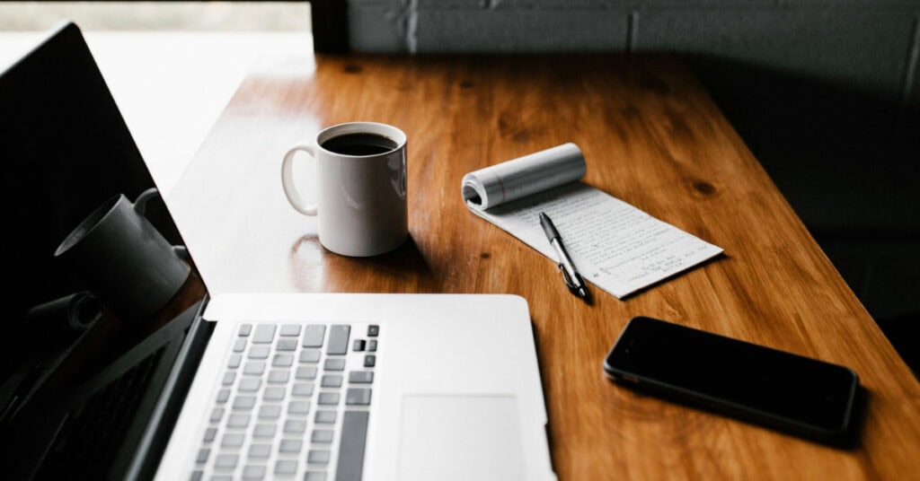 Laptop, coffee, notepad, and smartphone on a wooden desk, symbolizing ideas, learning, and small business insights.